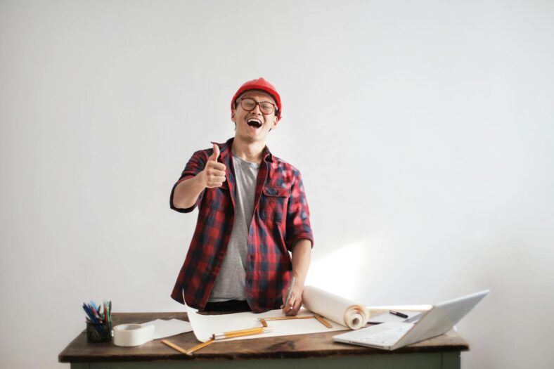 laughing male constructor showing thumb up at working desk